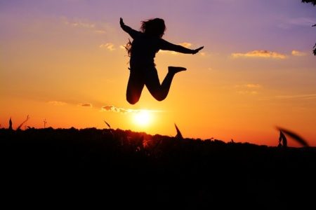 いいことがあって夕陽に向かってジャンプしている女性